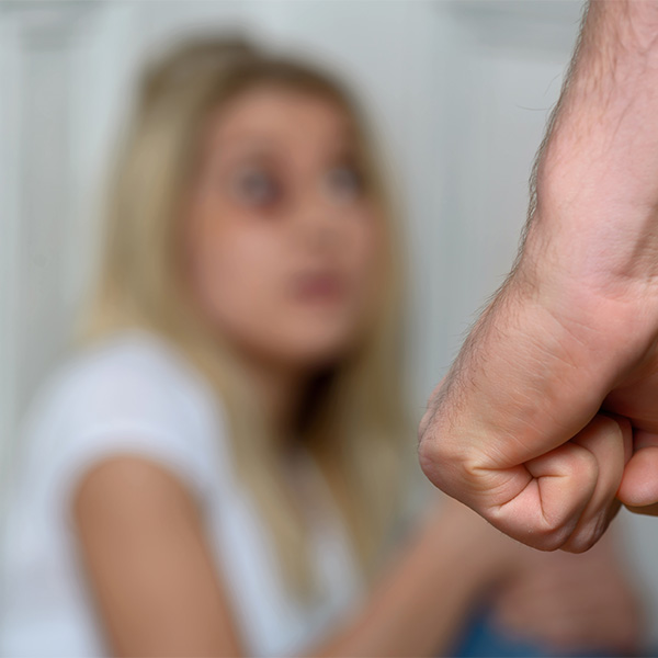 Fist of a man going to chastise the girl sitting on the floor in the corner